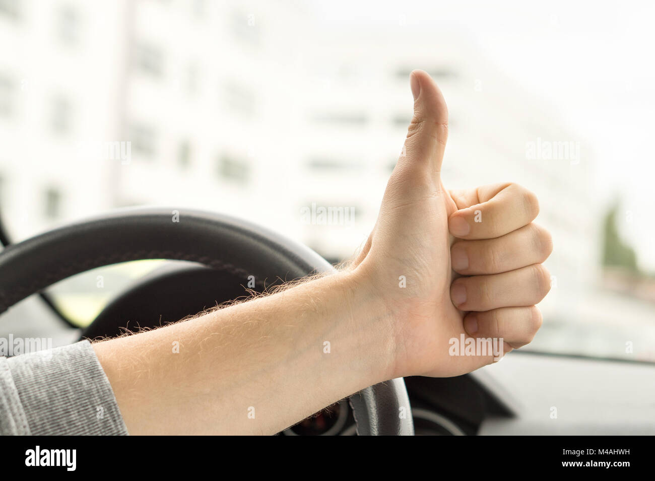 Feliz conductor mostrando Thumbs up en coche. Satisfecho con el coche nuevo o sin tráfico. Pasados test autoescuela o inspección del vehículo. Vehículo fijo. Foto de stock