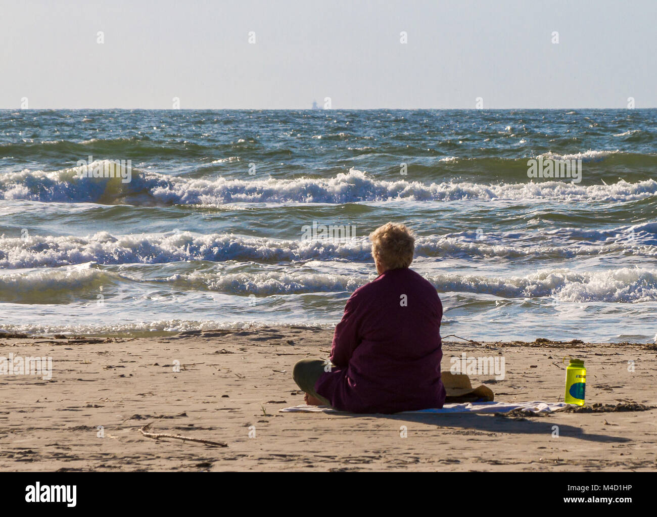 Un estadounidense senior citizen mujer sentada en la playa y mira el océano en el sol por la mañana temprano. Foto de stock