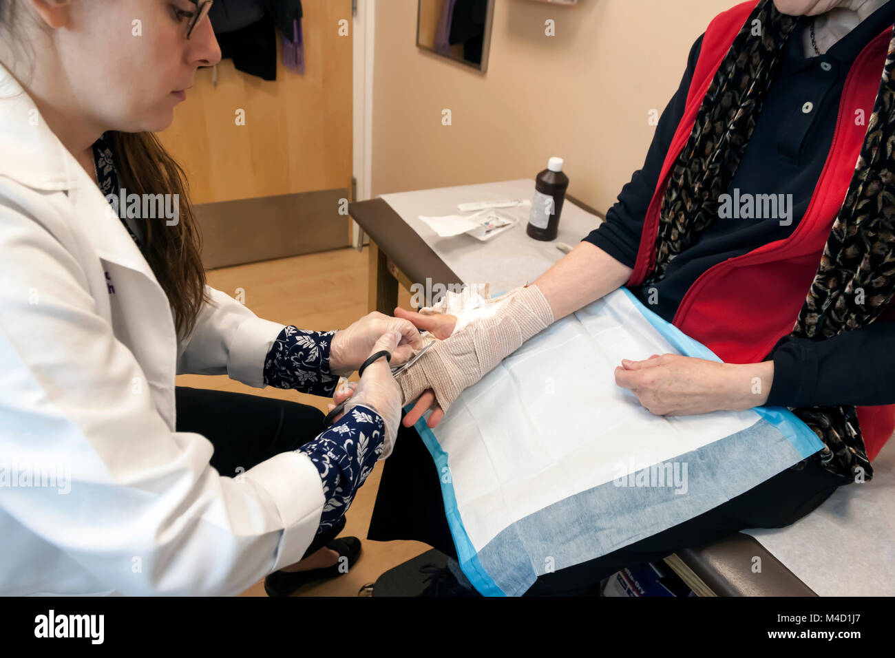Ayudante del Médico de corte y extracción de un vendaje de la mano del paciente un mes después de la cirugía La Contractura de Dupuytren. Foto de stock