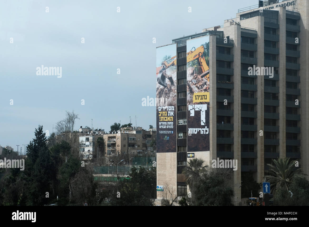 Un enorme cartel expuesto fuera de un hotel muestra una excavadora demoliendo una casa con un escrito 'Netanyahu, suficiente destrucción' en Jerusalén Occidental, Israel, el 15 de febrero de 2018. El gobierno israelí intenta posponer la remoción de algunas de las casas en el puesto avanzado Nativ Ha'avot oficialmente una expansión del asentamiento judío de Elazar en el grupo de asentamientos Gush Etzion en Cisjordania a pesar de la decisión de la Corte Suprema. Crédito: Eddie Gerald/Alamy Live News Foto de stock