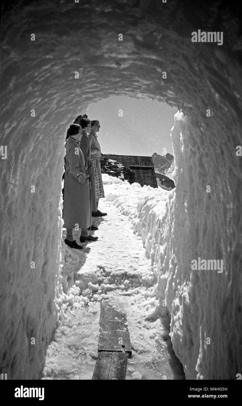 Vista desde la entrada de una cueva de hielo sobre un grupo de viajeros en un glaciar de los Alpes Suizos. Foto de stock