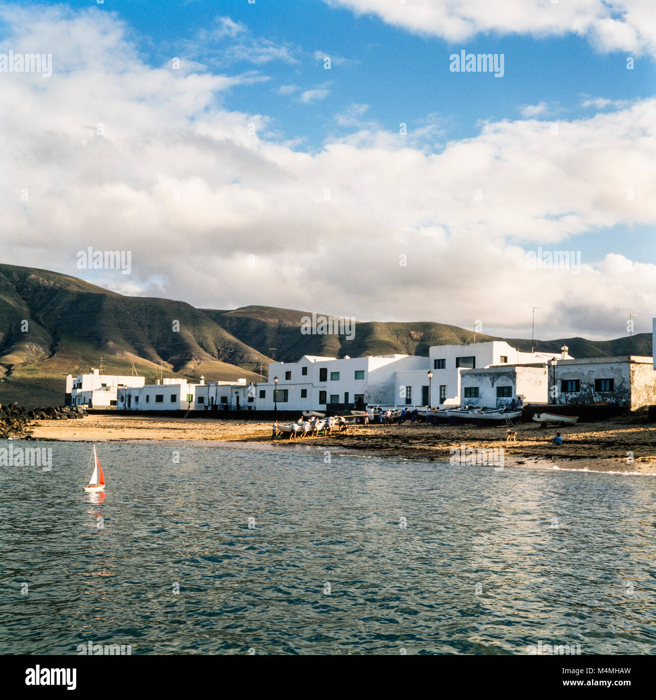 Juguete barco de vela en el mar mientras los aldeanos tirar de un barco de pesca en la playa, en una pequeña aldea, Lanzarote, Islas Canarias, España, archivo de fotografía de enero de 1988 Foto de stock