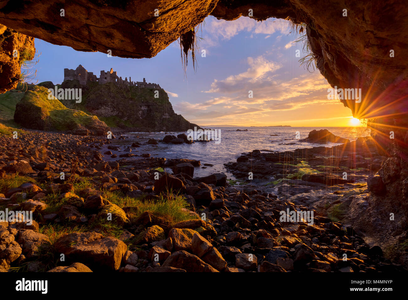 Castillo de Dunluce ocaso sobre el mar desde el interior de una cueva. Costa Causeway, Condado de Antrim, Irlanda del Norte. Foto de stock