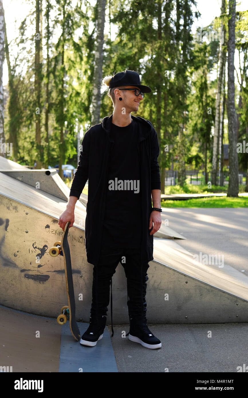 Hombre tatuado en ropa negra posando con el monopatín en el skate park  Fotografía de stock - Alamy