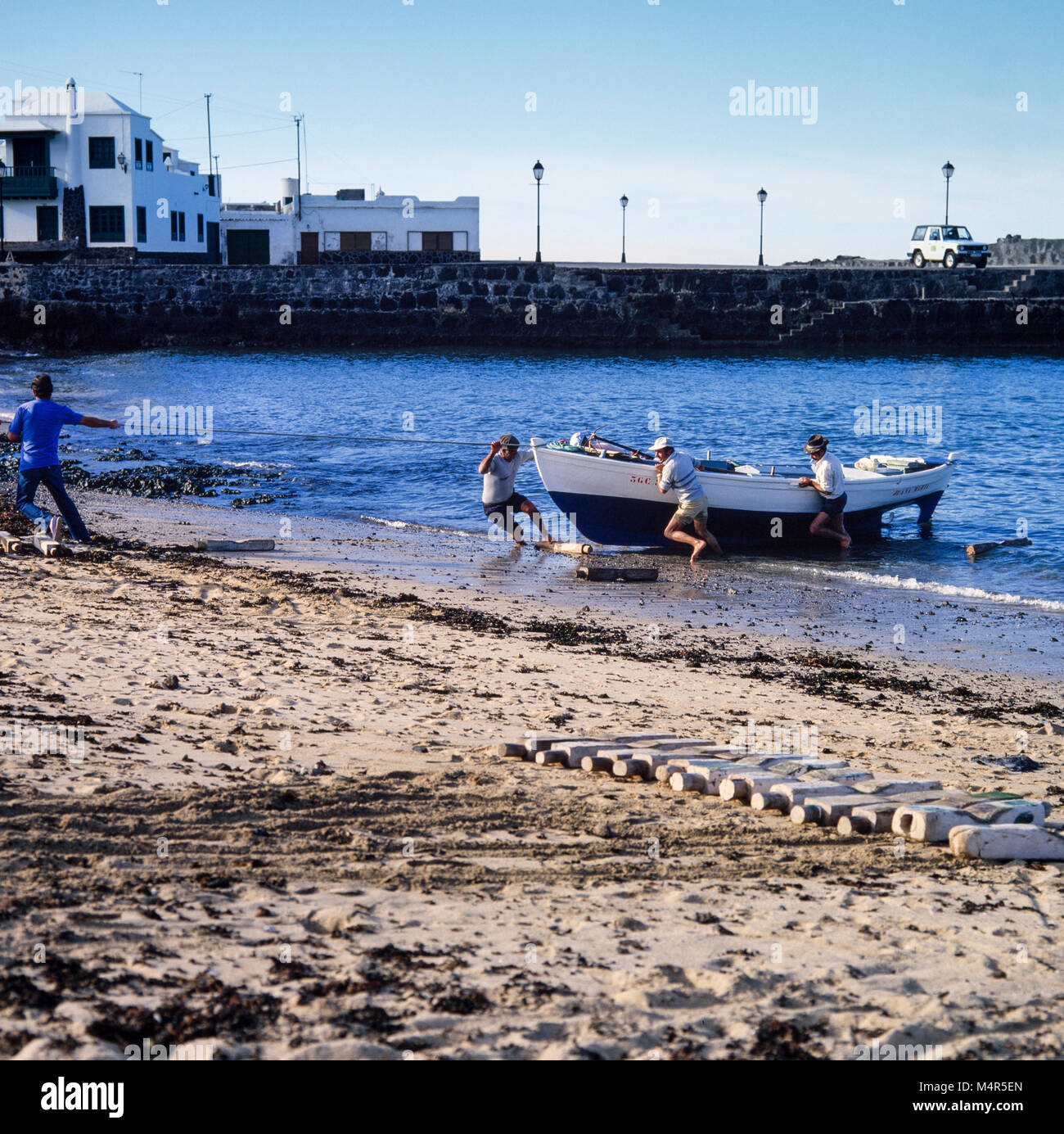 Los pescadores y familia, acarreando una embarcación desde el mar hasta la playa en Lanzarote, Islas Canarias, España, archivo de fotografía de enero de 1988 Foto de stock