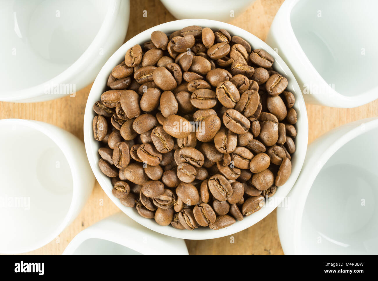 Los granos de café tostado ligeramente marrón rodeada por blanco tazas sobre una mesa de madera arriba Foto de stock