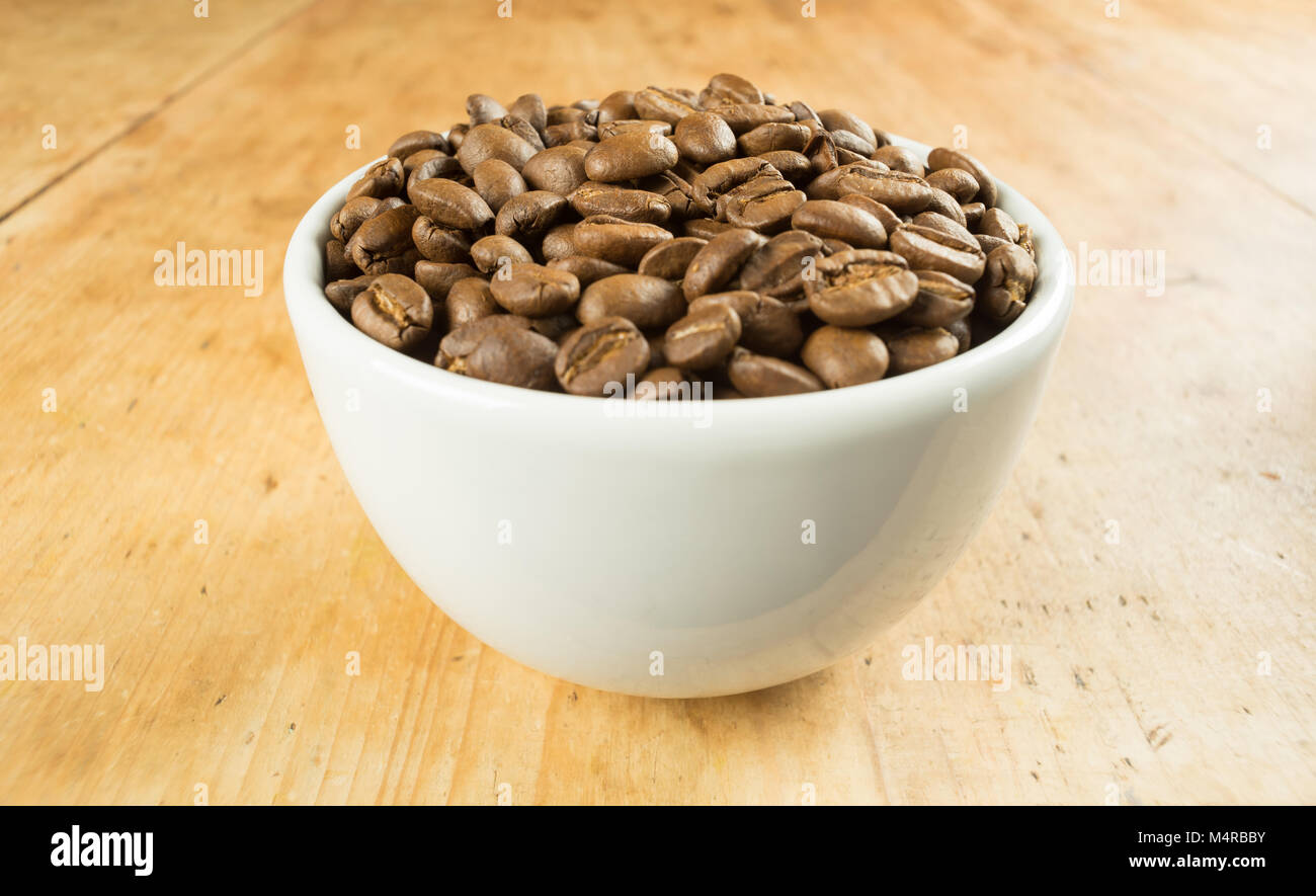Luz marrón tostado de granos de café en un recipiente blanco sobre una mesa de madera arriba Foto de stock