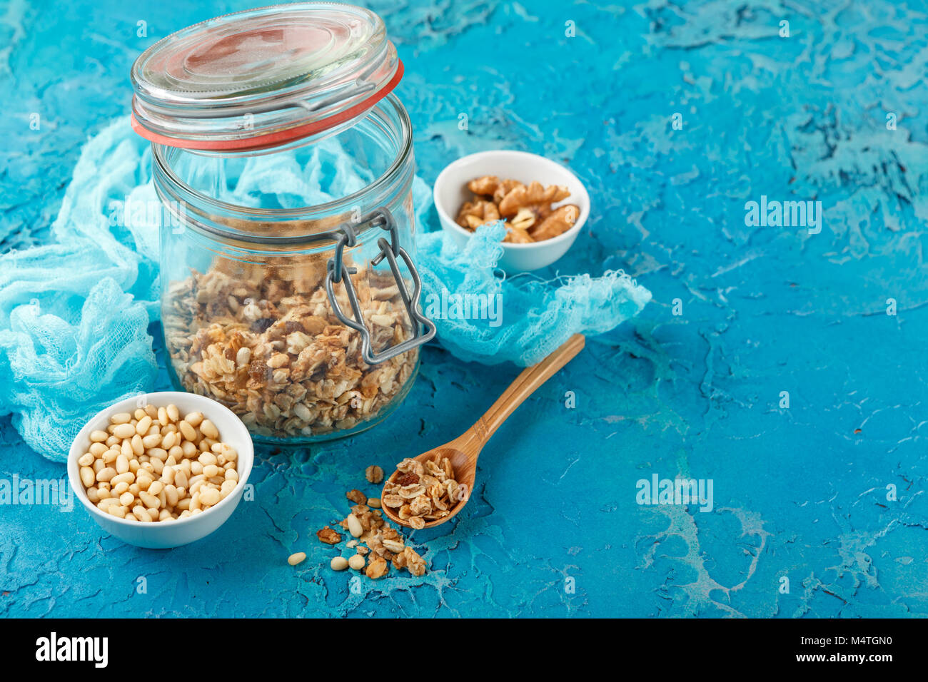 Granola casera en un frasco de vidrio y establecer diferentes tipos de frutos secos: Los cacahuetes en conchas, piñones sobre fondo azul. Foto de stock