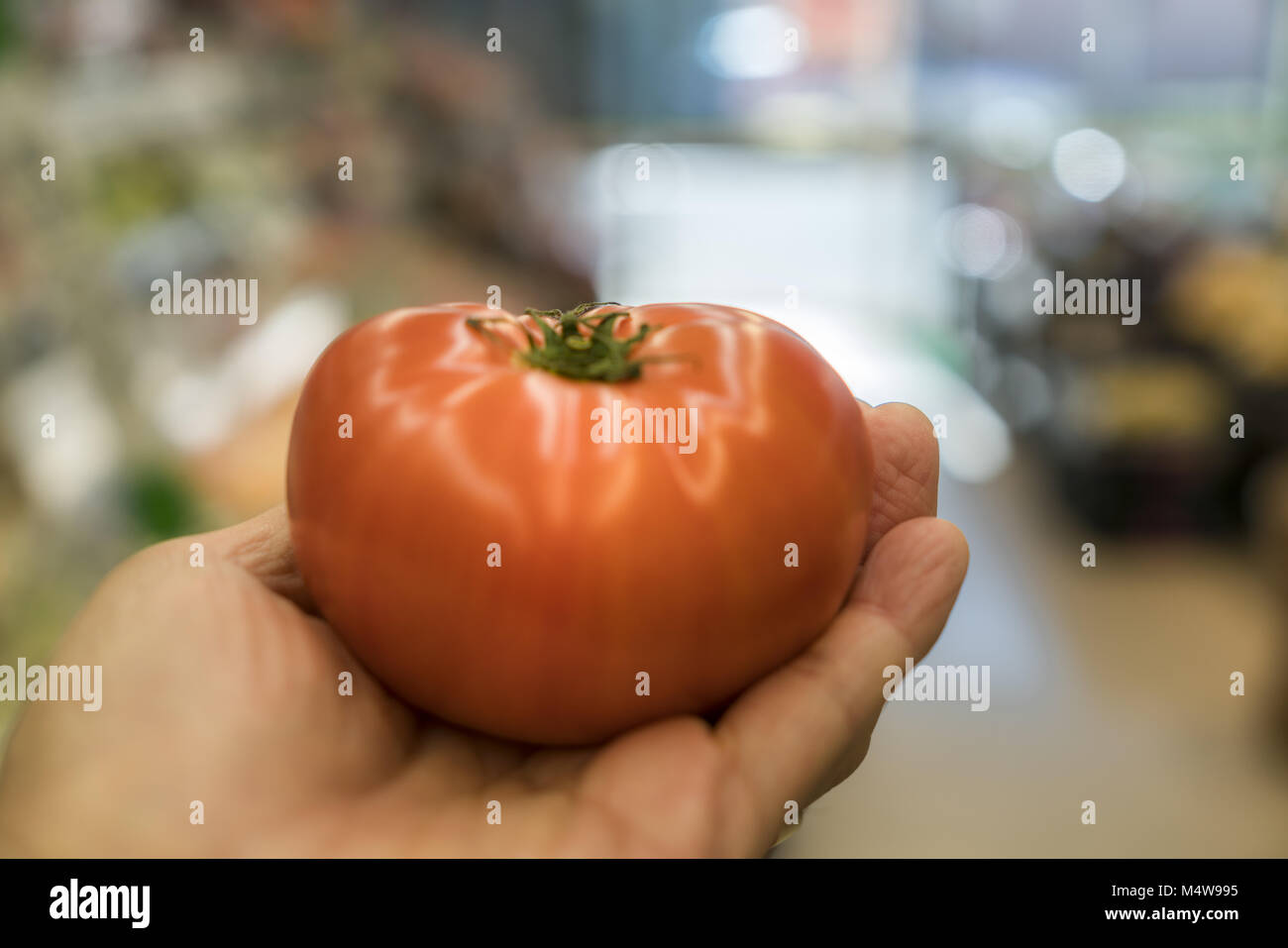 Una mano sujetando un tomate fresco en el supermercado Foto de stock