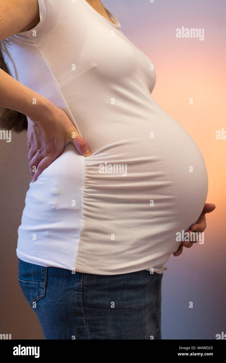 Una mujer embarazada fuertemente sosteniendo su espalda y su vientre Foto de stock