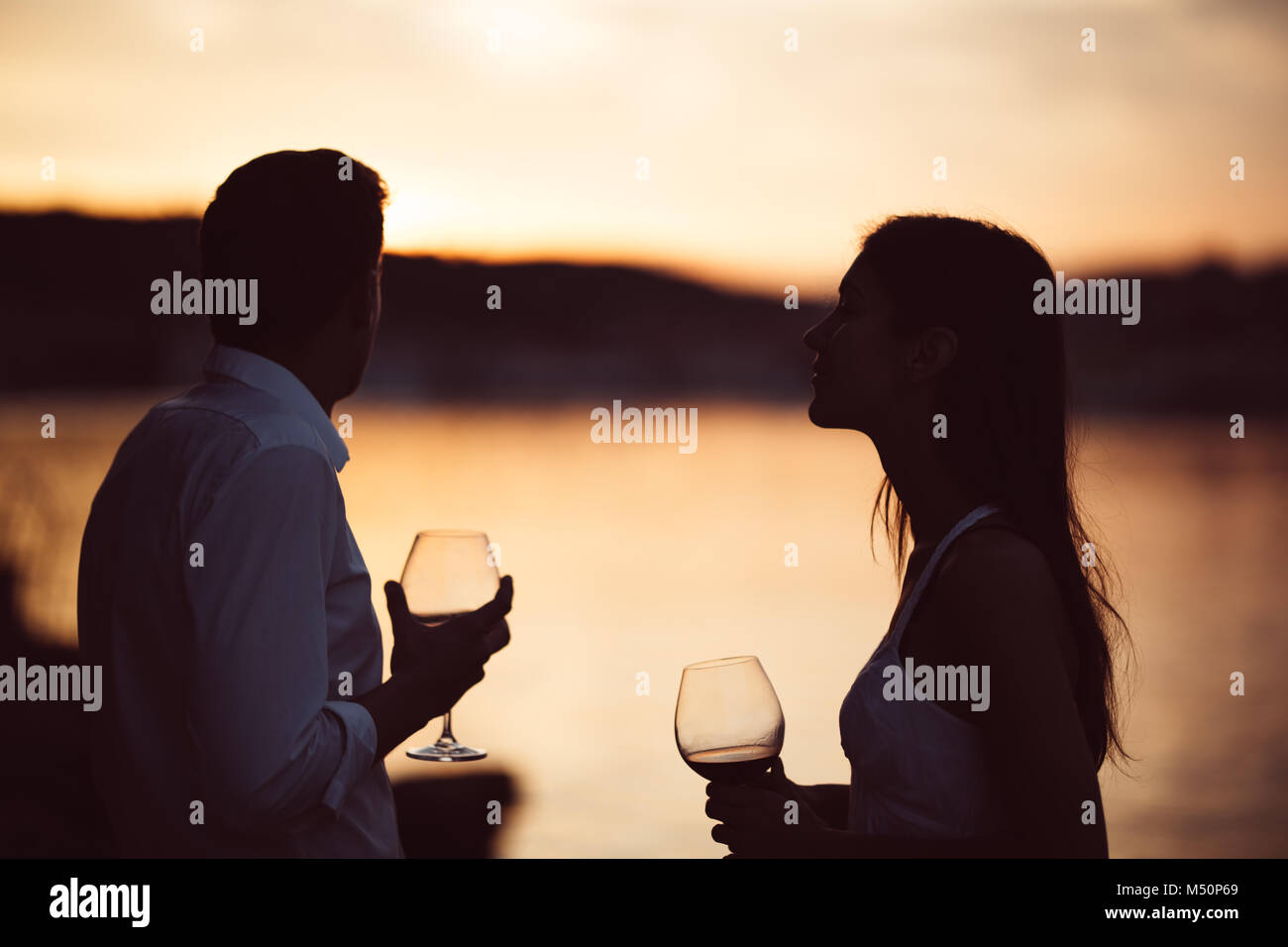 Dos jóvenes disfrutando de una copa de vino tinto en el atardecer en la playa.saludable vaso od vino tinto casero,cultura mediterránea.los climas cálidos,mares Foto de stock