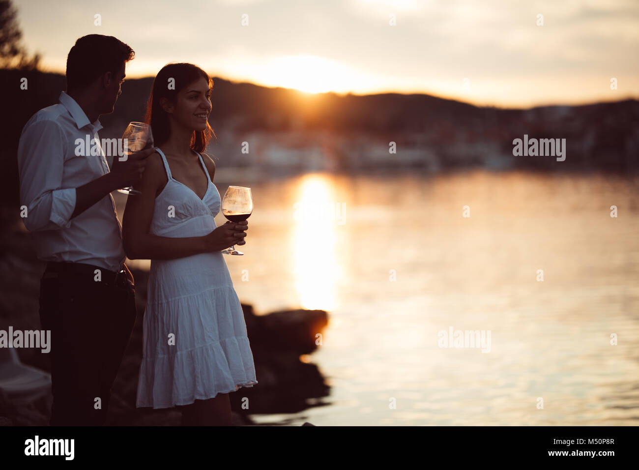 Dos jóvenes disfrutando de una copa de vino tinto en el atardecer en la playa.saludable vaso od vino tinto casero,cultura mediterránea.los climas cálidos,mares Foto de stock