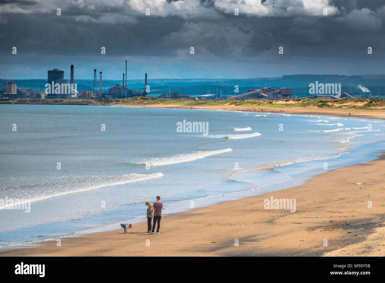 Una familia disfruta de una hermosa playa con industria pesada en el fondo. Foto de stock