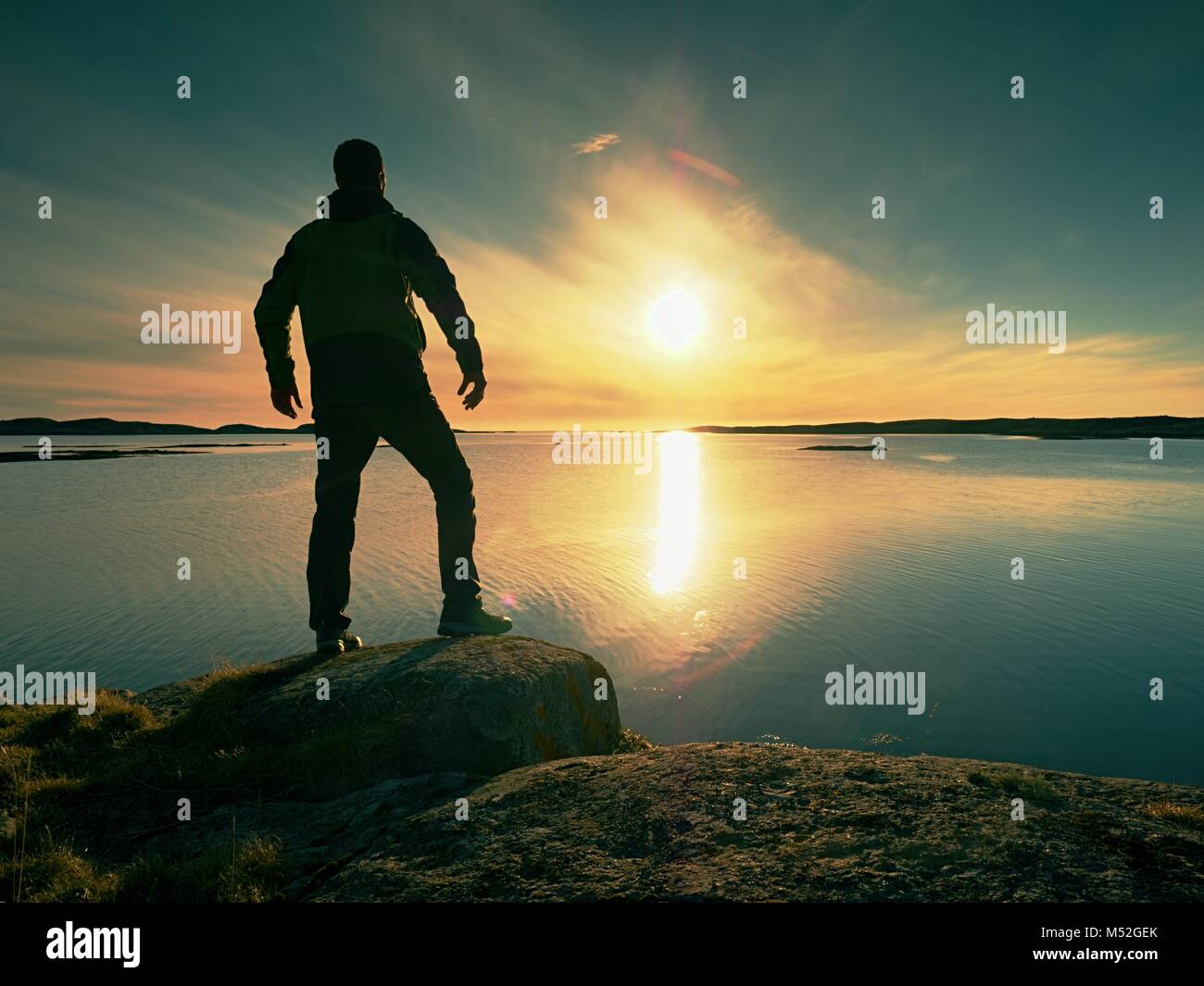 Silueta de un hombre en ropa de calle en acantilado rocoso sobre el mar. Hikerthinking durante la puesta de sol en el fondo. Concepto de viaje lejos. Foto de stock