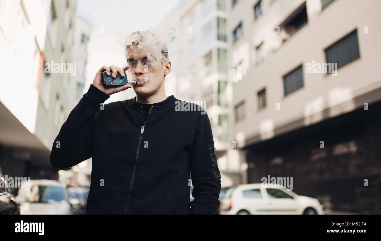 Joven con cigarrillo electrónico para fumar en lugares públicos.La restricción de humo,la prohibición de fumar.Usando vaping dispositivo con un líquido saborizado.E-juice vaping. Foto de stock