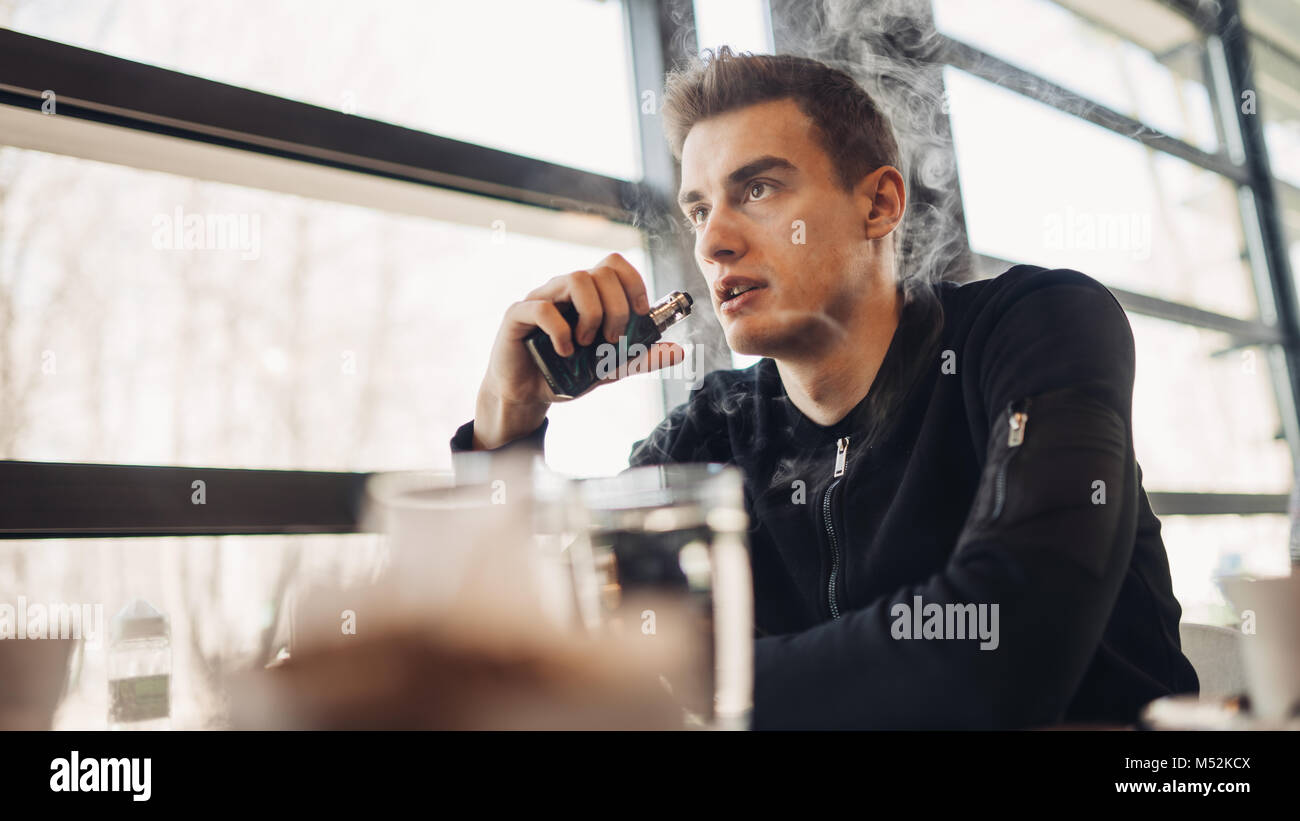 Joven vaping cerrada en el espacio público.Fumar cigarrillo electronico en cafe.La adicción a la nicotina.Forma para dejar de fumar,viejo hábito.Vaping aroma,hombre urbano u Foto de stock