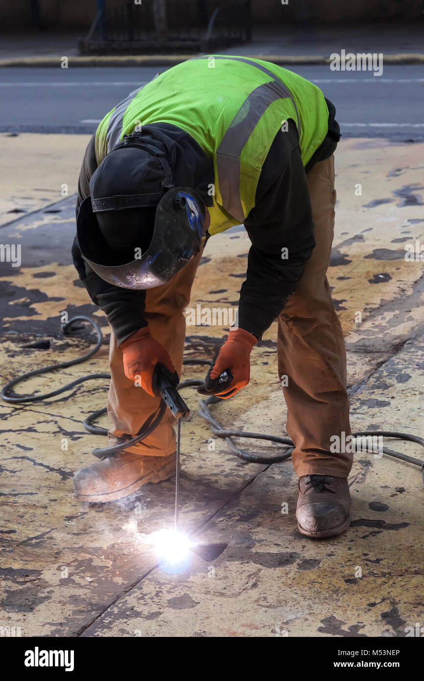 Un trabajador de soldar una placa de acero en una calle de la ciudad de Nueva York. Foto de stock