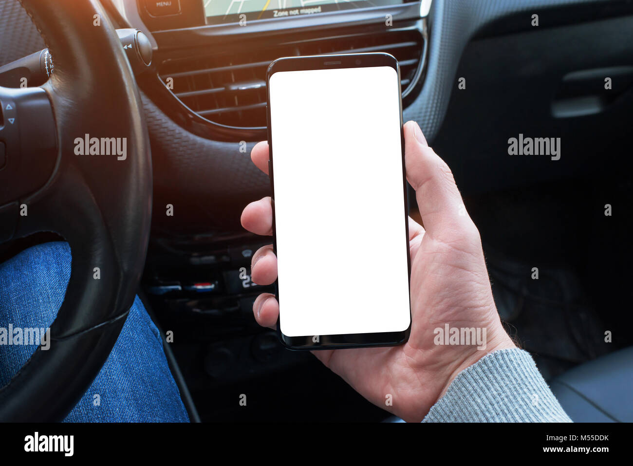 Teléfono inteligente con pantalla aislados de boceto en el conductor del coche de la mano. Cerca. Volante y coche interior en segundo plano. Foto de stock