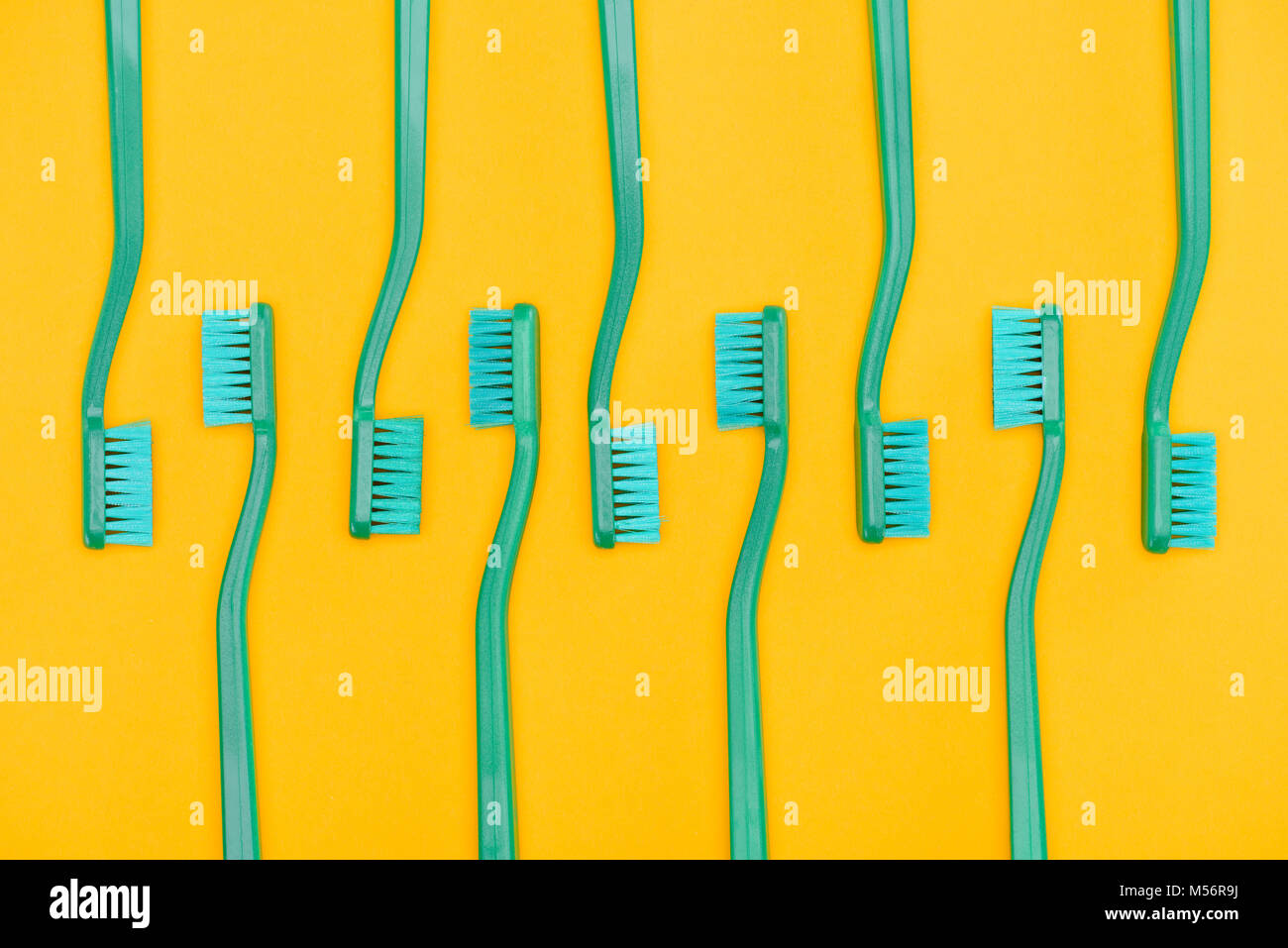 Minimalista con fondo verde cepillos de dientes en fila, aislado en amarillo Foto de stock
