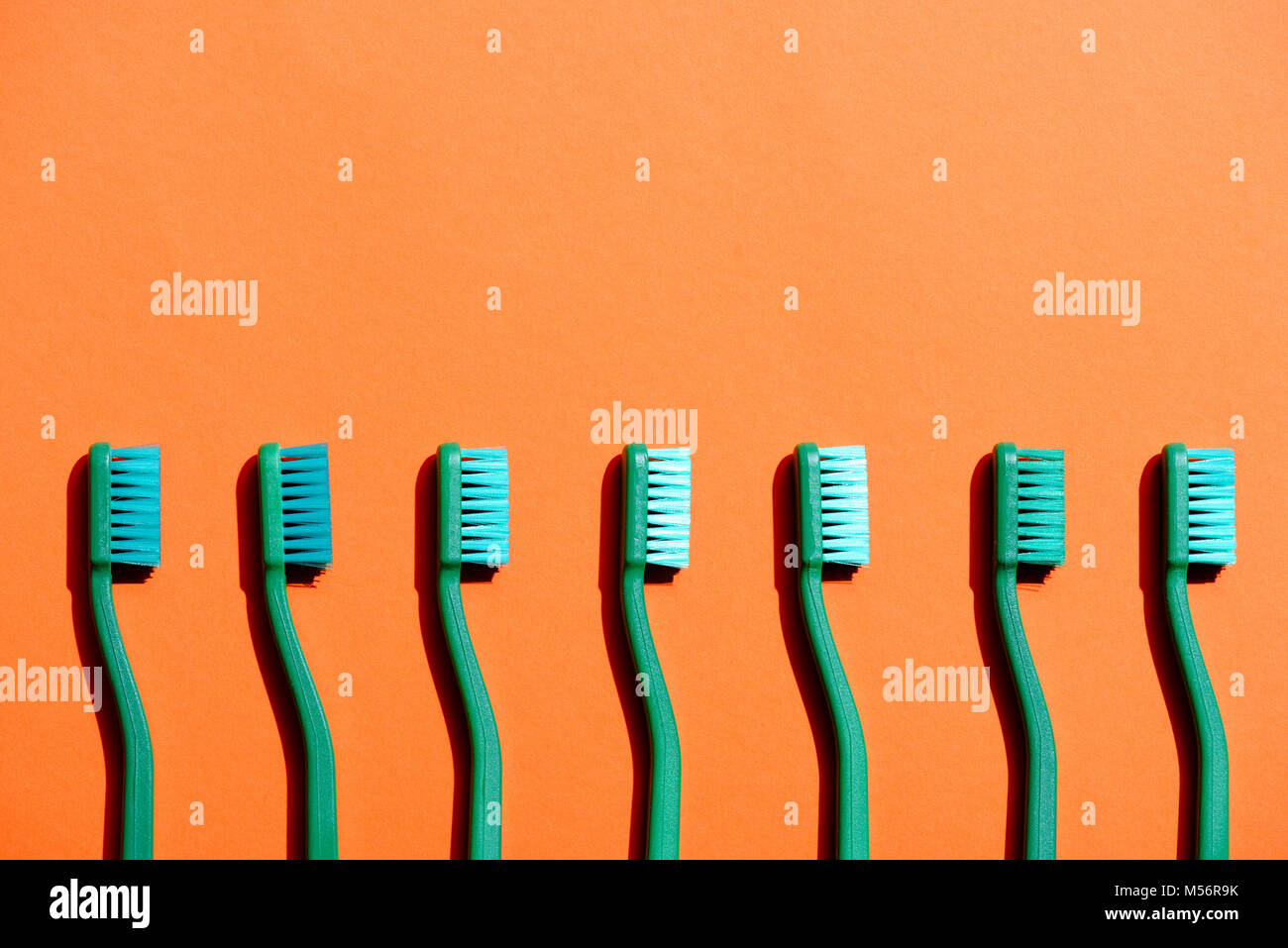 Cepillos de dientes verde en fila, en naranja con espacio de copia Foto de stock
