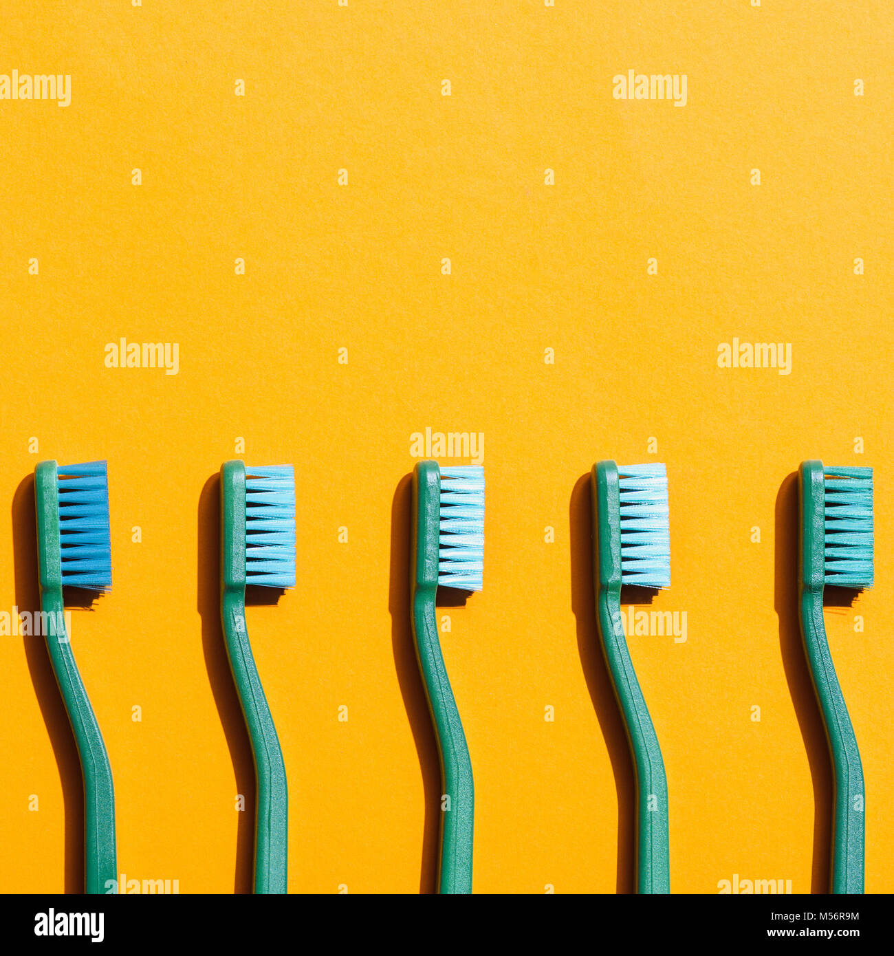 Cepillos de dientes verde en fila, en amarillo con espacio de copia Foto de stock