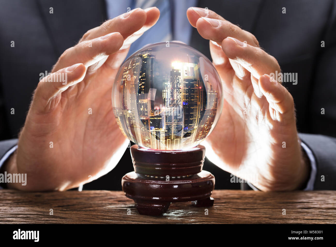 Parte media del empresario cubriendo bola de cristal con paisaje urbano en mesa de madera Foto de stock
