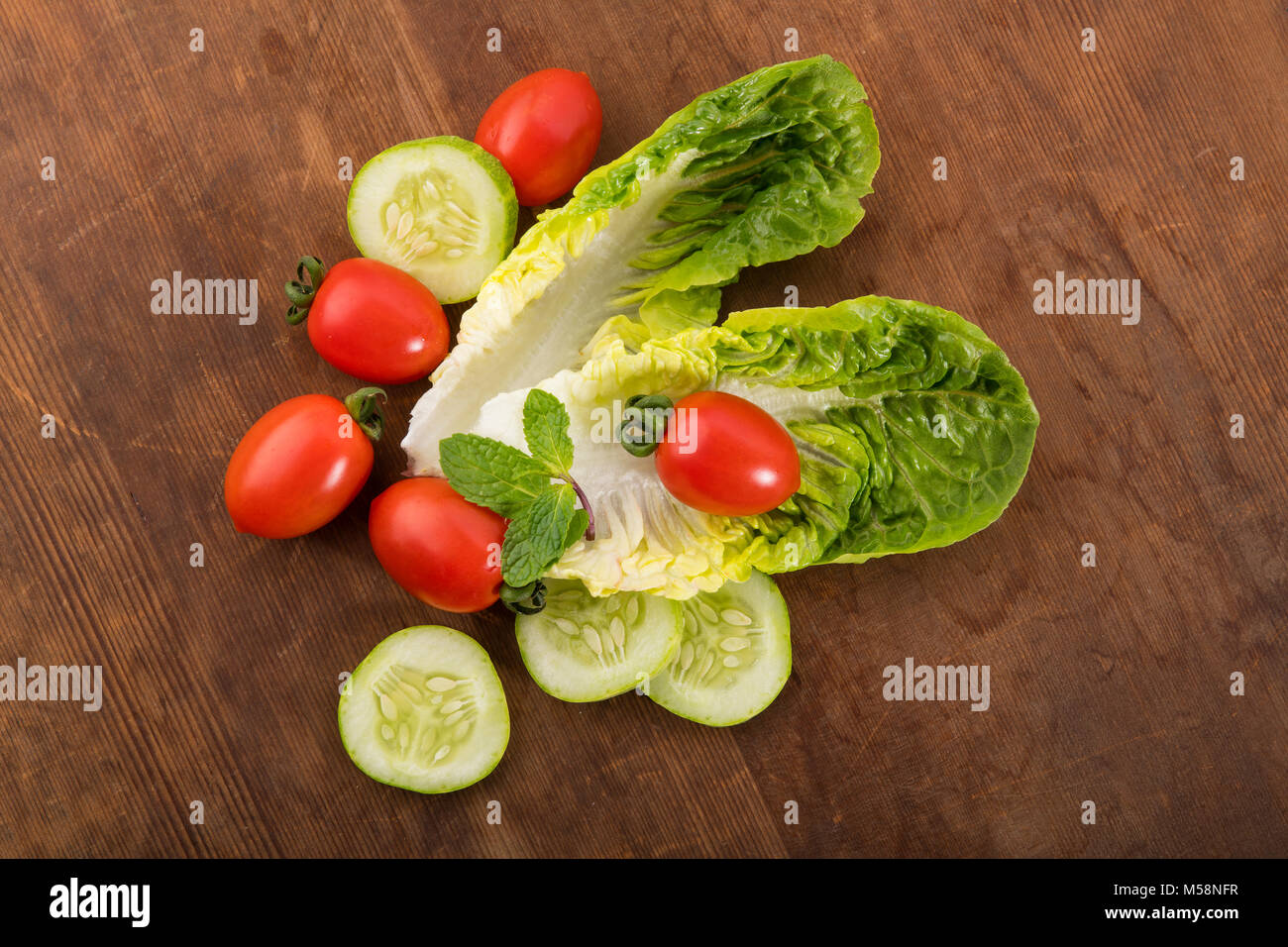 Verdura: fresco verde lechuga romana con el bebé los tomates, hojas de menta y rodajas de pepino sobre fondo de madera marrón Foto de stock