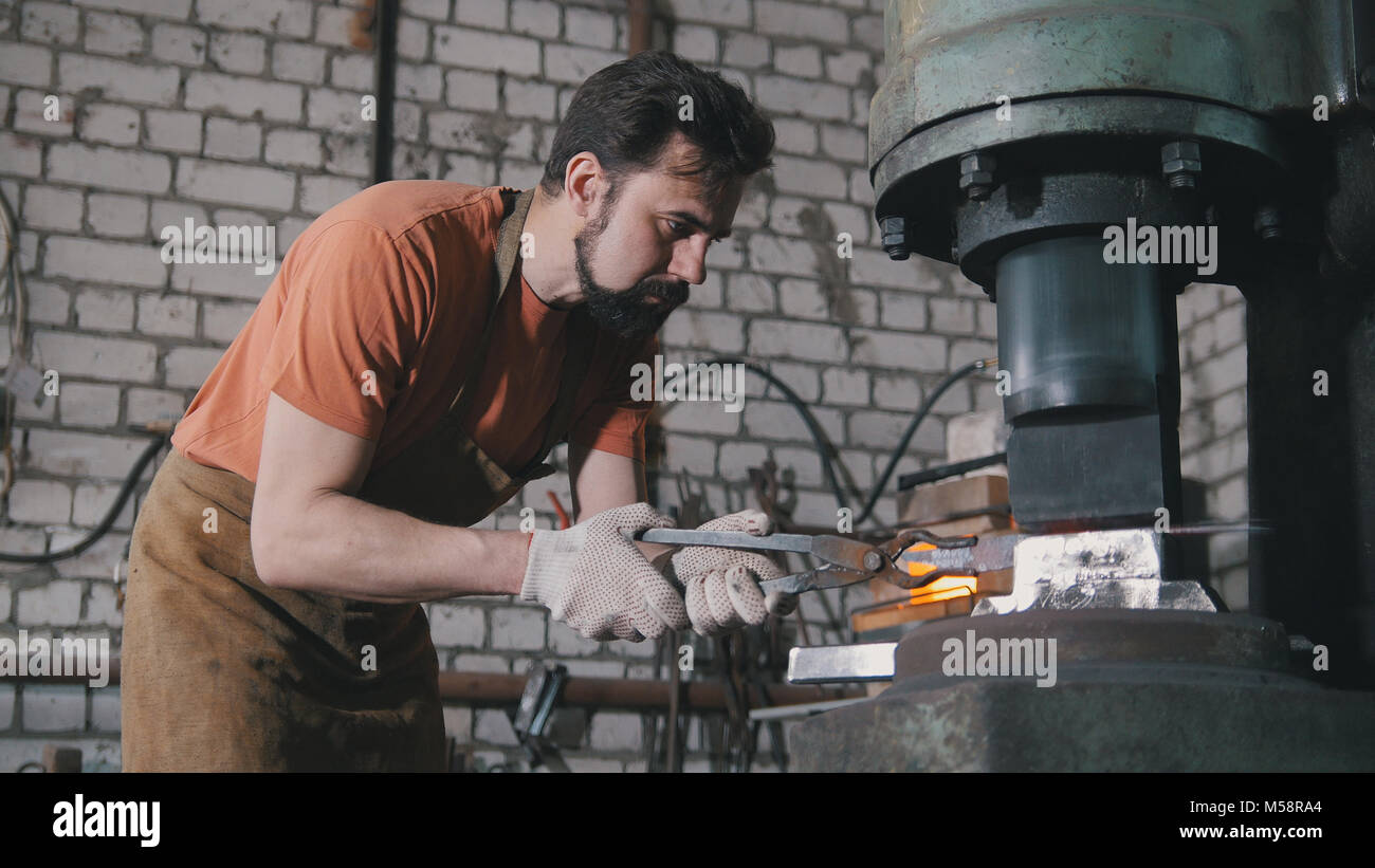 Hombre herrero en el taller de forja de hierro caliente rojo sobre el yunque - small business Foto de stock