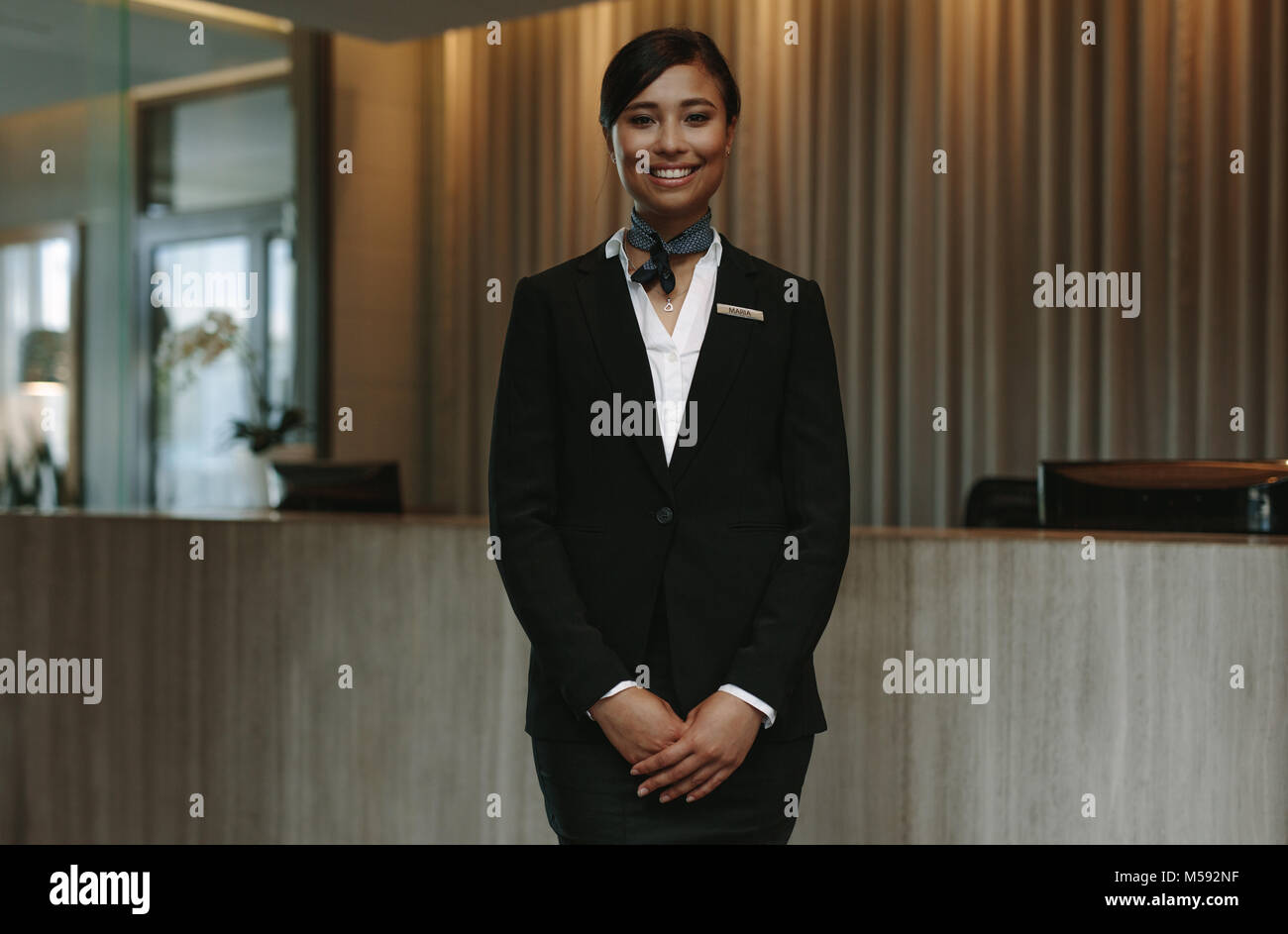 Feliz hembra sonriente recepcionista en el hotel. Hermosa conserje en uniforme esperando para dar la bienvenida a los huéspedes. Foto de stock