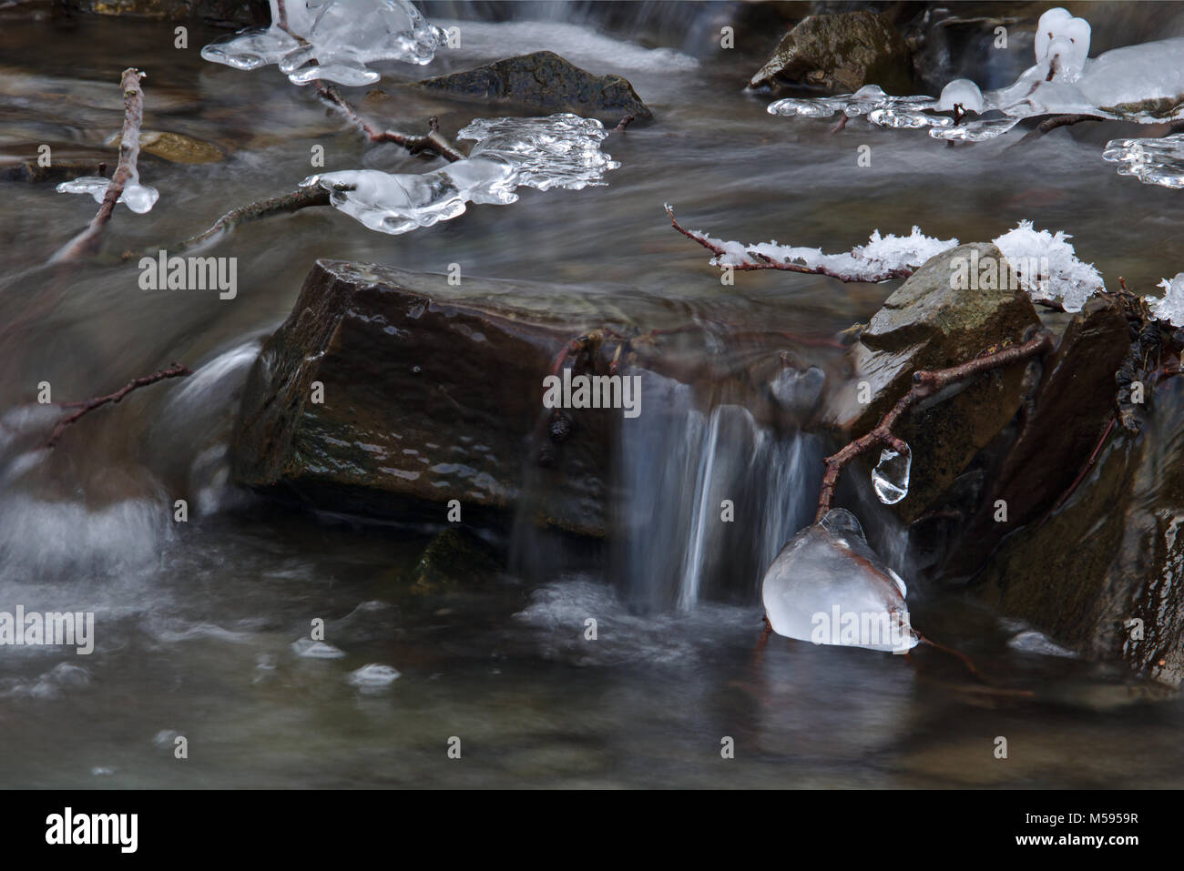 El agua que fluye por encima de una roca en un arroyo con pequeños trozos de hielo (larga exposición) Foto de stock