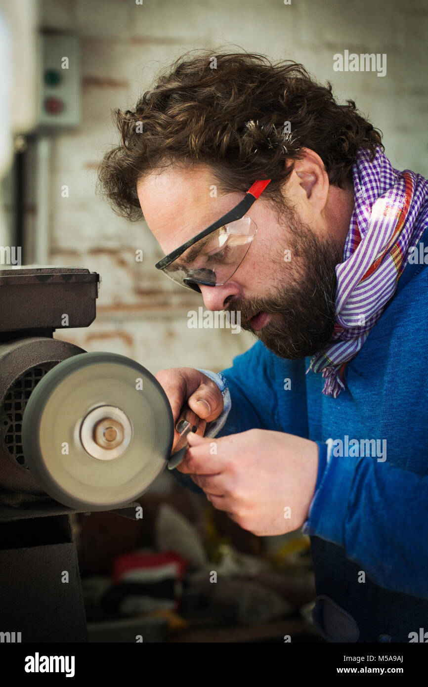 Un artesano en el trabajo afilando la hoja de un cuchillo con una  rectificadora plana, una rueda giratoria para templar y afinar el borde  cortante Fotografía de stock - Alamy