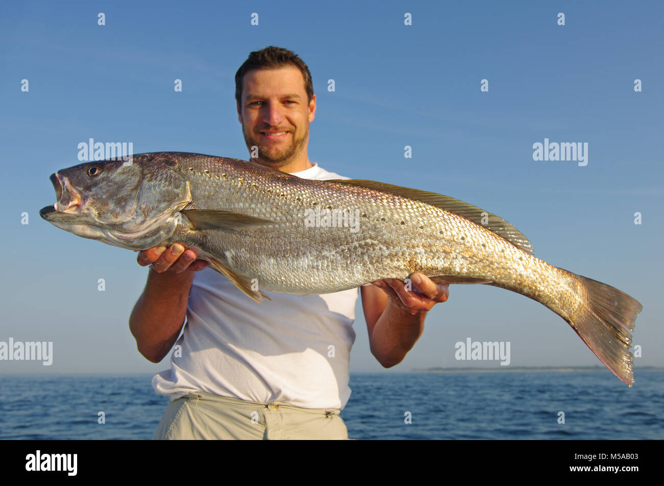 Lucky fisherman sosteniendo un gran pez de agua salada Foto de stock