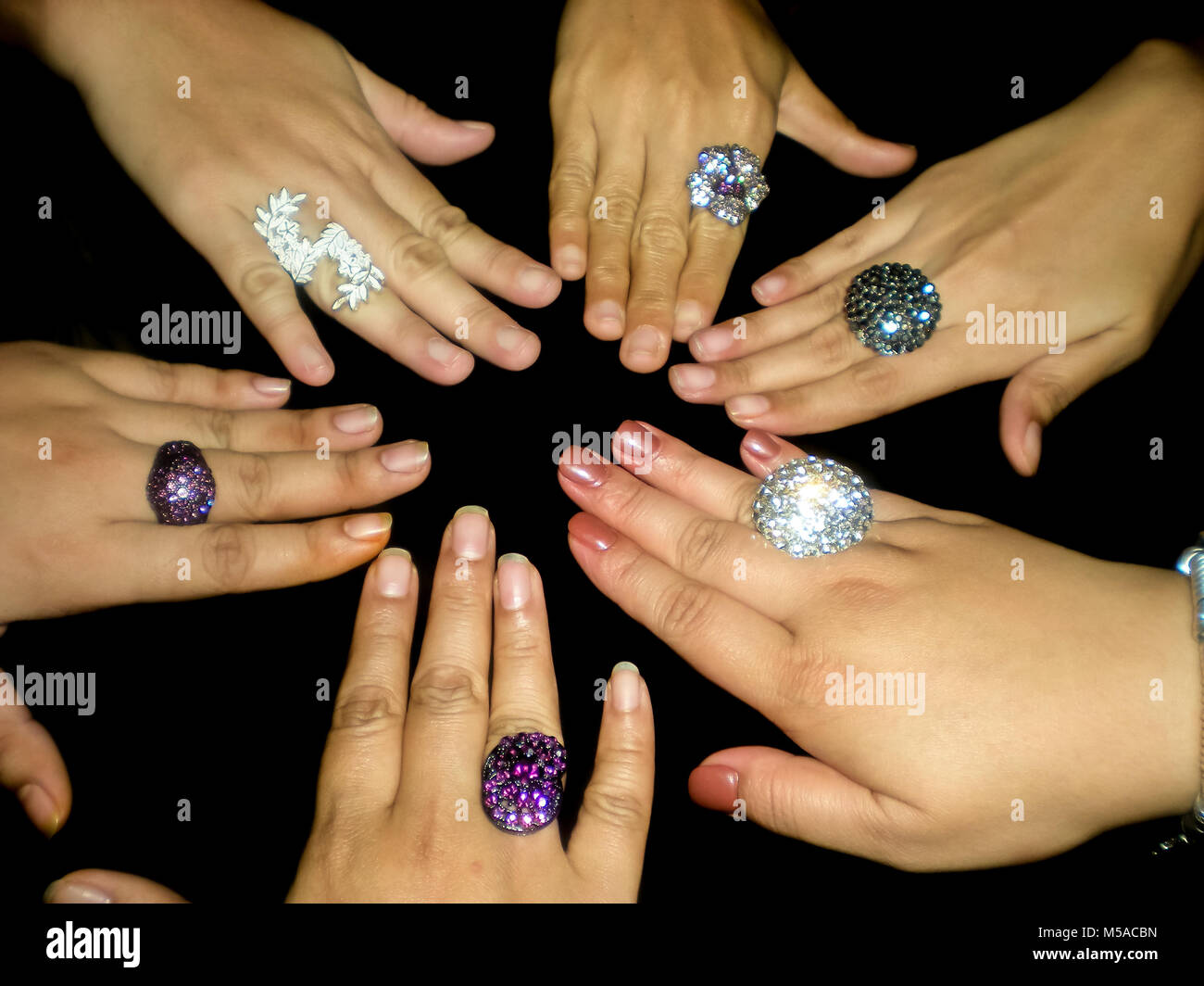 Manos femeninas contra un fondo oscuro, todos luciendo grandes anillos de  bisutería Fotografía de stock - Alamy