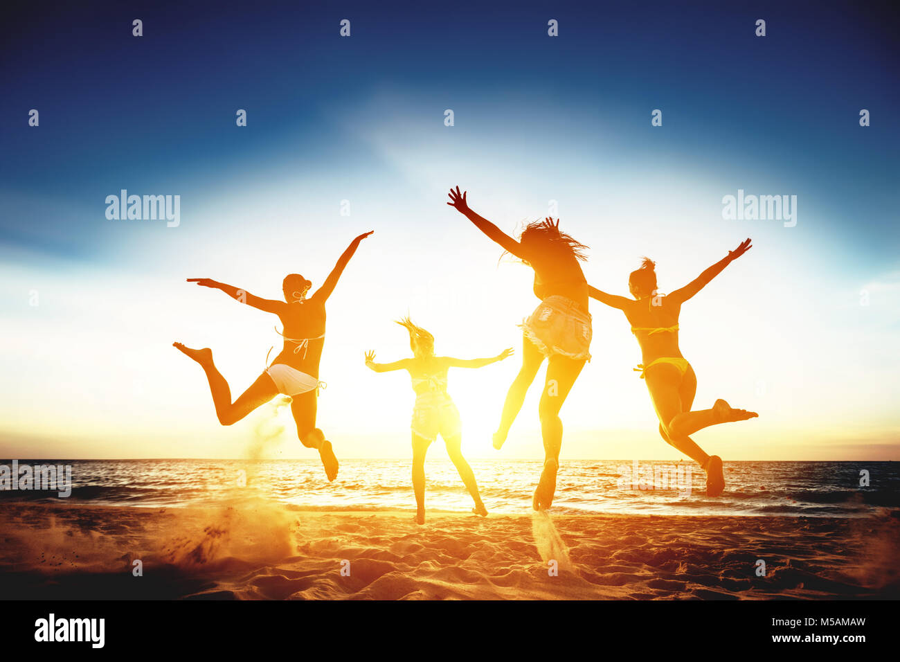 Cuatro niñas feliz correr y saltar contra el mar al atardecer Foto de stock