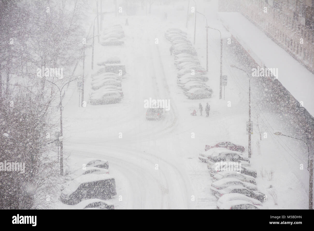 Panorama urbano de la ciudad en tiempo de invierno en la tormenta de nieve con algunas personas, snowcovered automóviles en una carretera, quitanieves, ambulancia Foto de stock