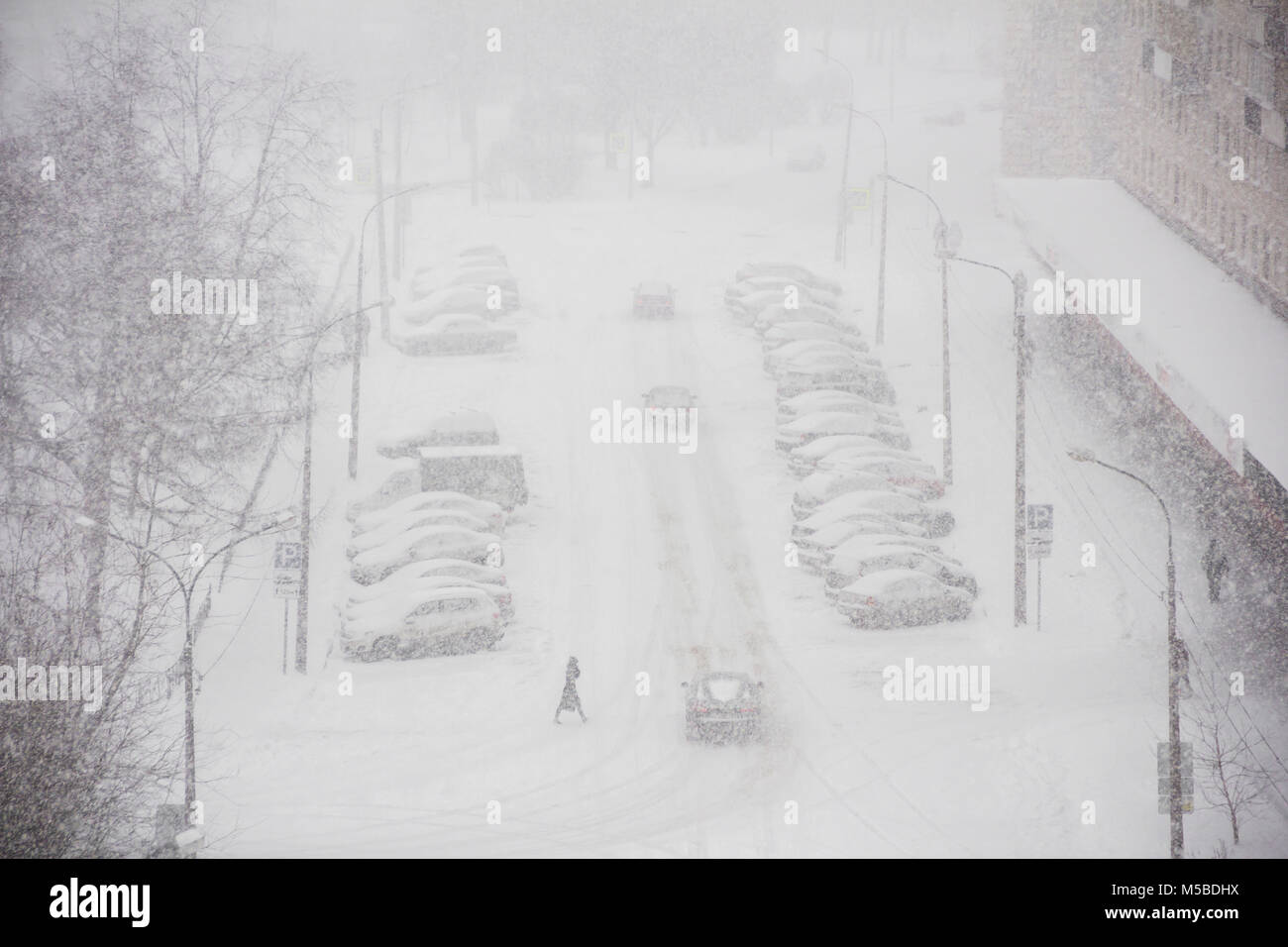 Panorama urbano de la ciudad en tiempo de invierno en la tormenta de nieve con algunas personas, snowcovered automóviles en una carretera, quitanieves, ambulancia Foto de stock