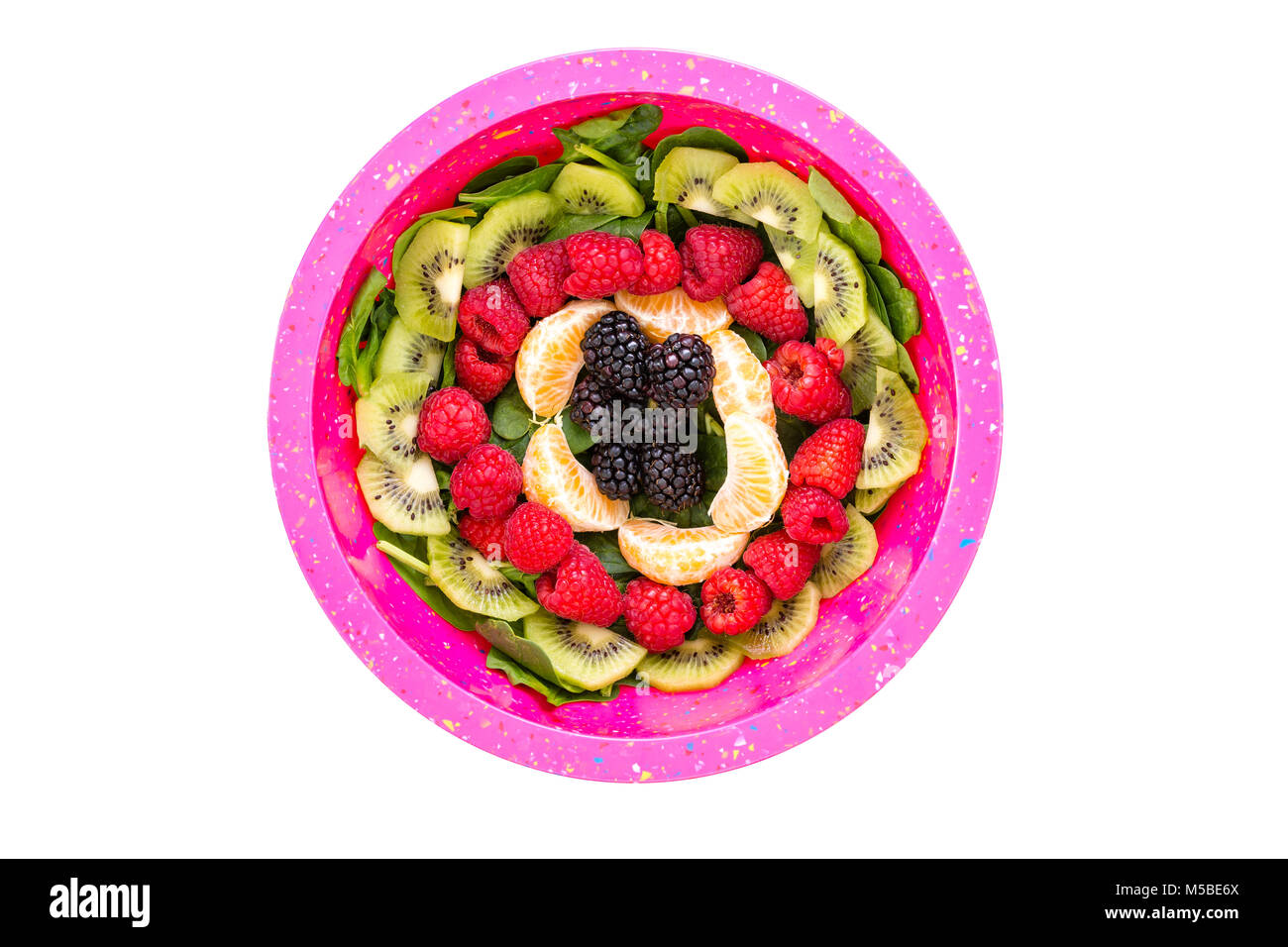 Ensalada de espinacas bebé rematado con fruta fresca perfectamente dispuestas en círculos concéntricos visto desde arriba con kiwi, frambuesas, moras y segmentos Foto de stock