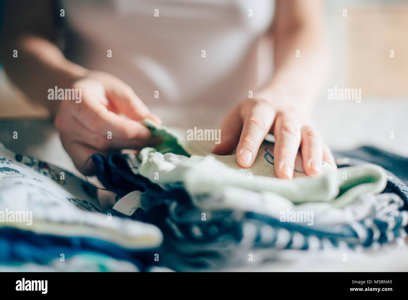 Clasificación madre bebé ropa para planchar en casa como parte de su rutina diaria en el cuidado de los niños, el enfoque selectivo Foto de stock