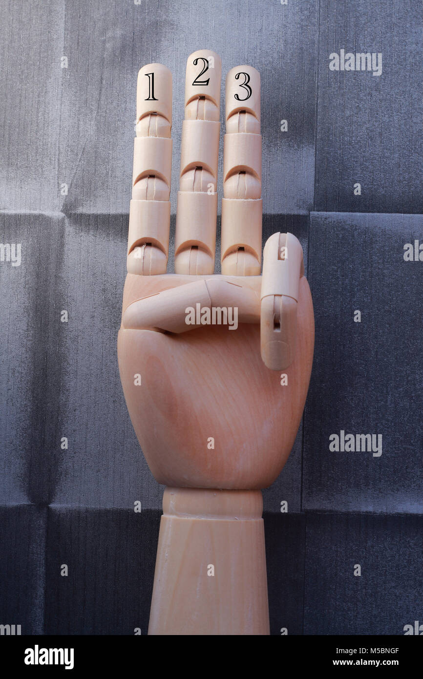 Mano de madera con tres dedos planteadas y numeradas con números uno, dos y tres, sobre un fondo de papel tapiz vintage Foto de stock
