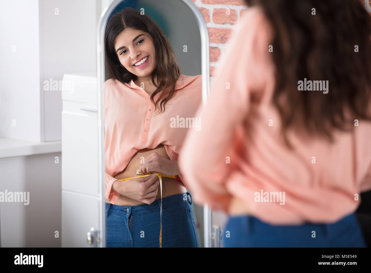 Reflejo de una mujer alegre y la medición de la cintura con una cinta. Foto de stock