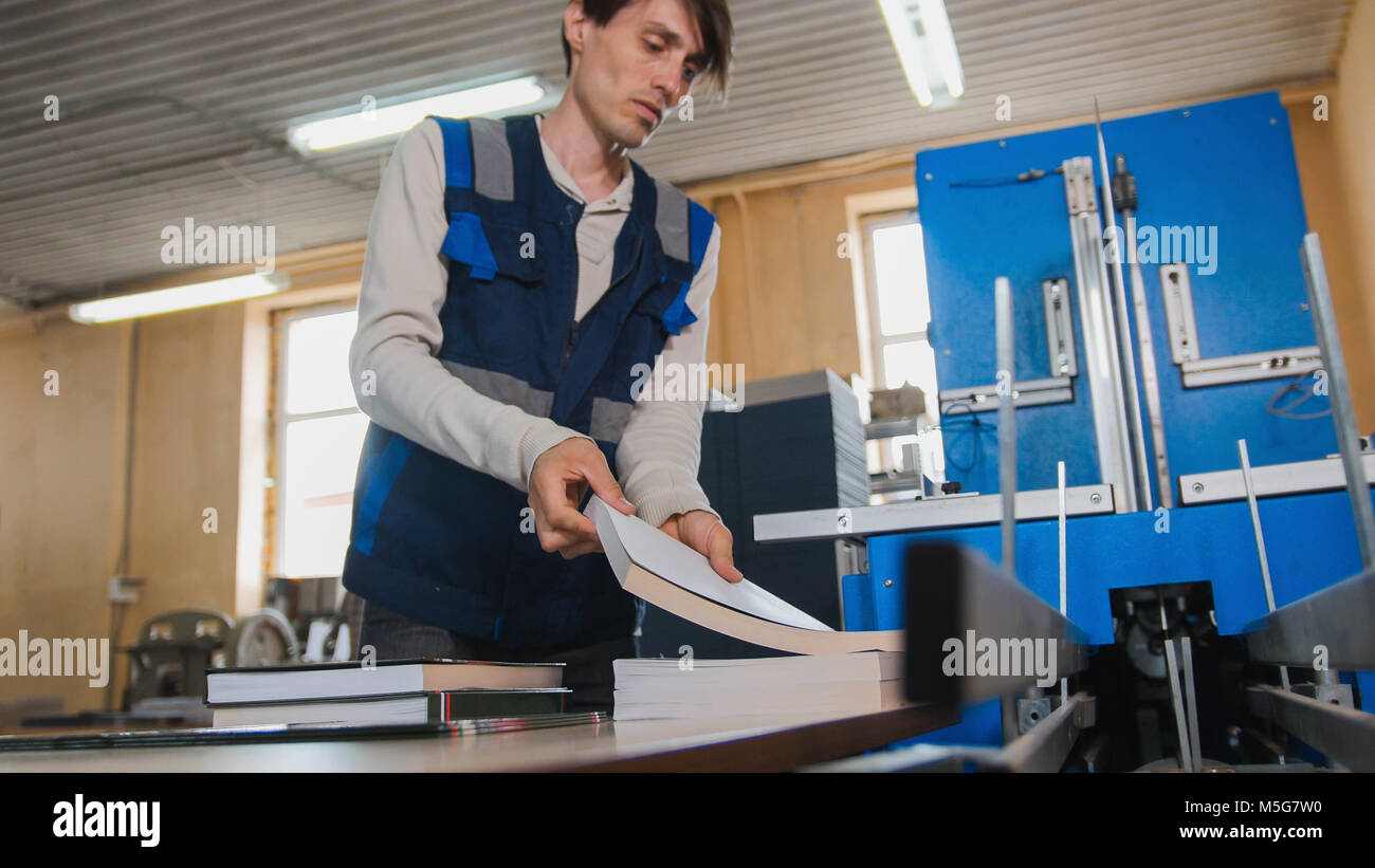 Trabajador inserta hojas de papel para la máquina de impresión, industria POLIGRAFO Foto de stock