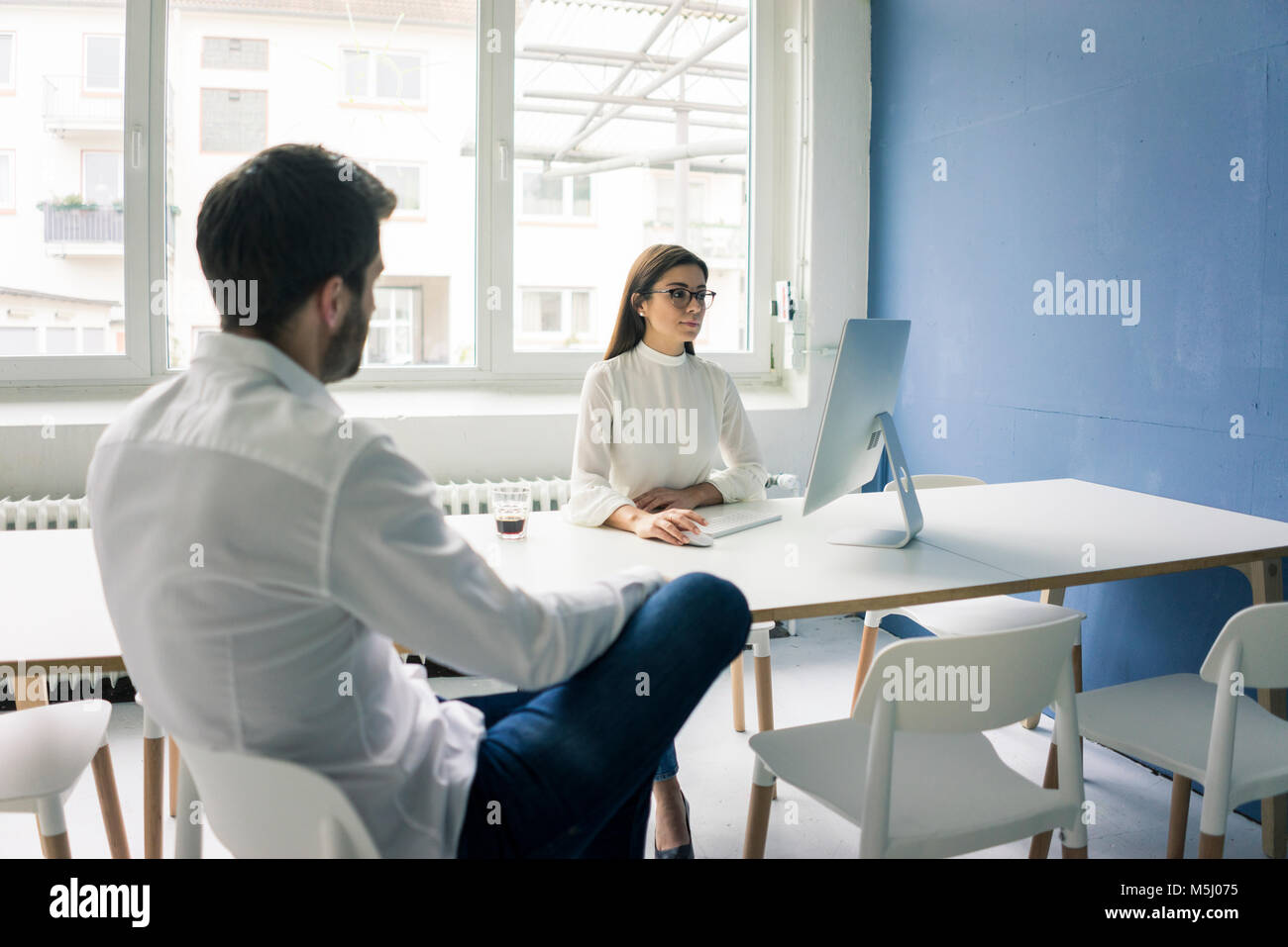 Hombre sentado frente a la mujer que usa equipo de oficina Foto de stock