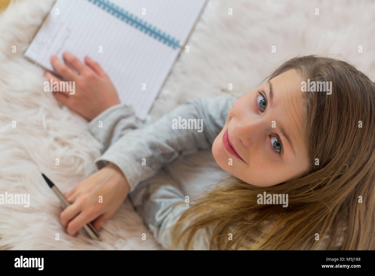 Retrato de niña sonriente tumbado en el suelo con un lápiz y un folleto Foto de stock