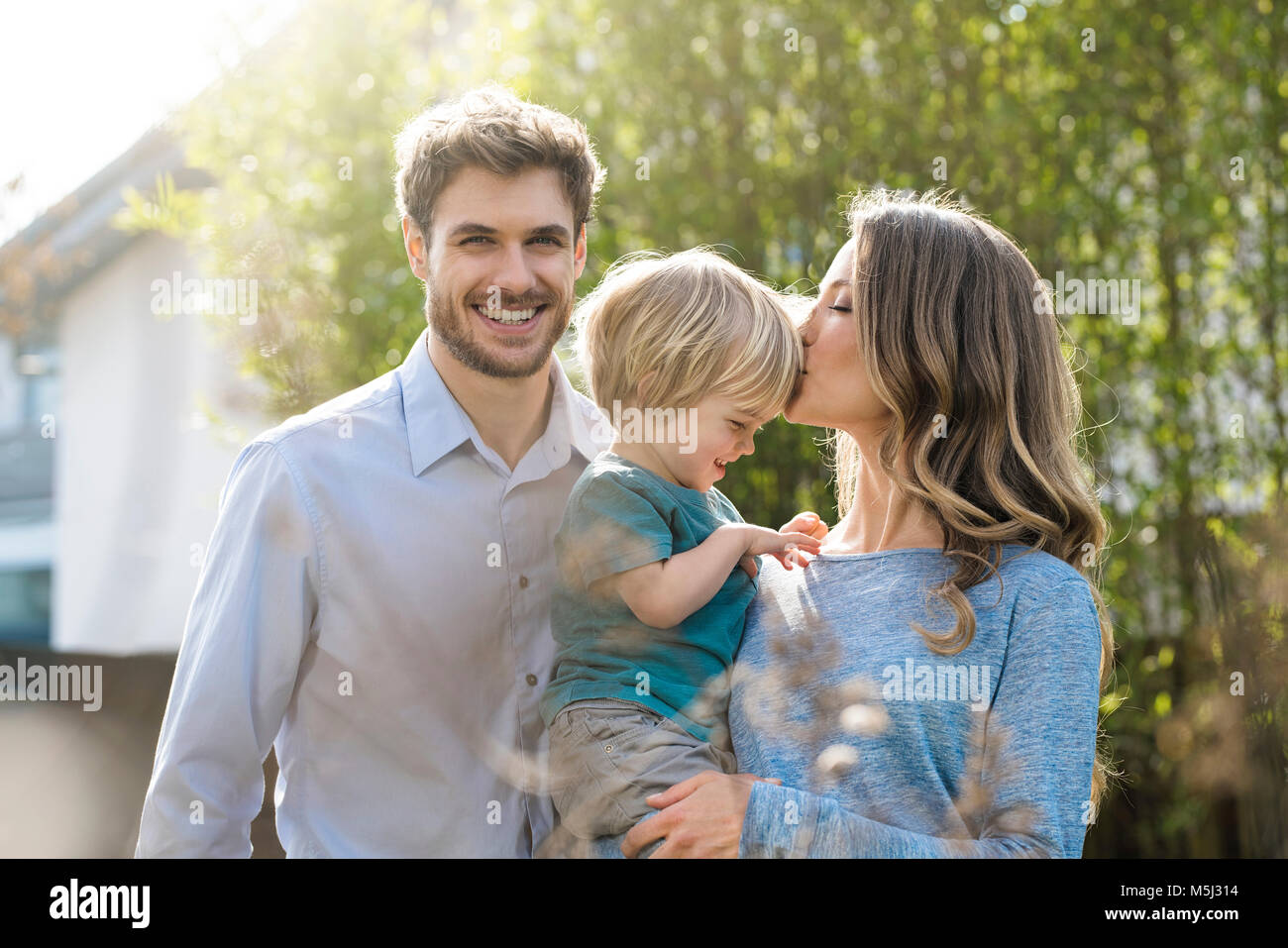 Familia Feliz en el jardín de enfrente de plantas de bambú con besos madre hijo Foto de stock