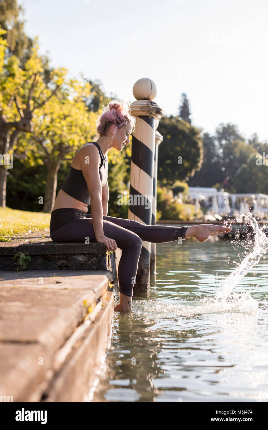 Mujer en ropa deportiva en Lakeshore sentado con los pies en el agua Foto de stock