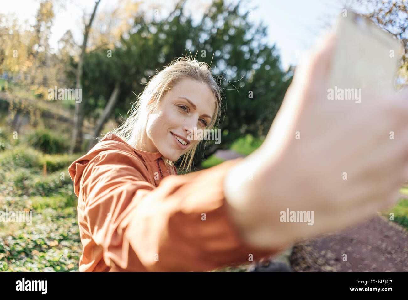 Retrato de mujer joven tomando selfie con teléfono celular en parque otoñal Foto de stock