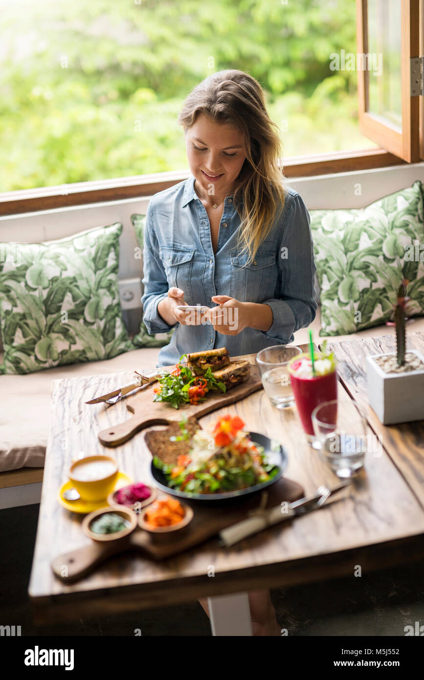 Mujer toma una imagen de los alimentos con el smartphone en el acogedor café en frente de la ventana Foto de stock