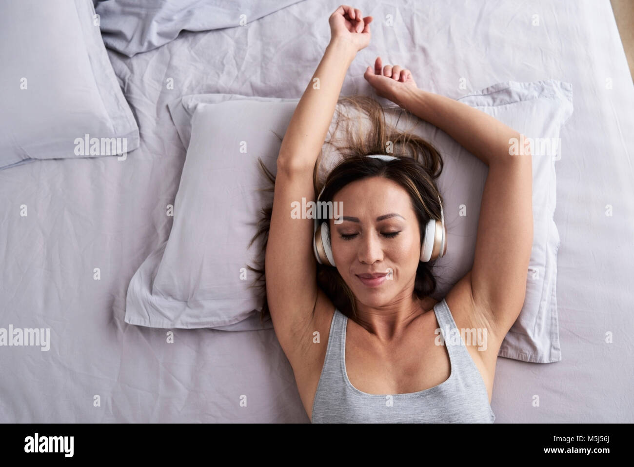 Bonita mujer asiática escuchando música con auriculares en la cama. Darme la música. Foto de stock