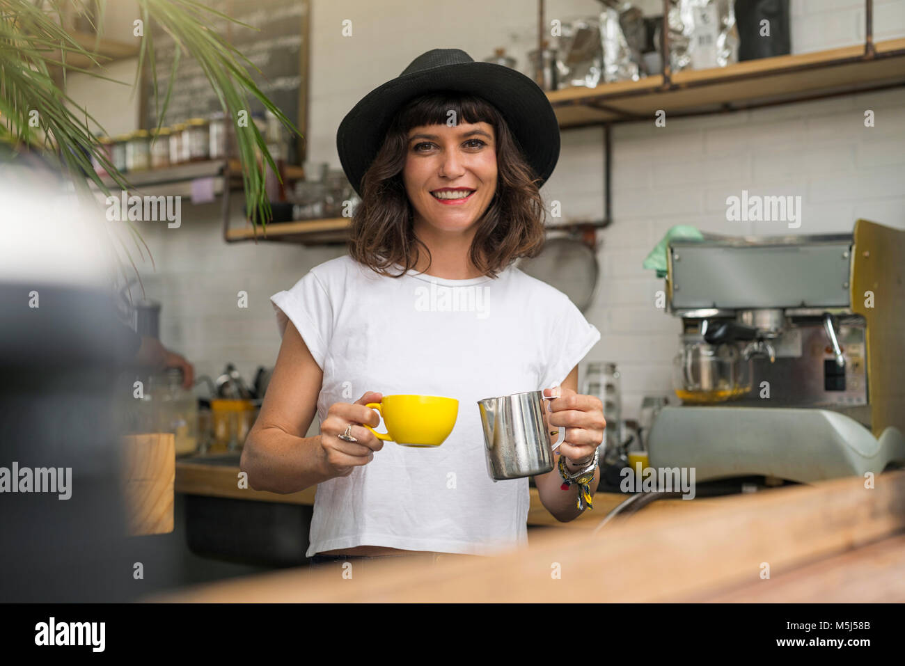 Retrato de mujer con sombrero negro detrás de la barra preparando un café Foto de stock