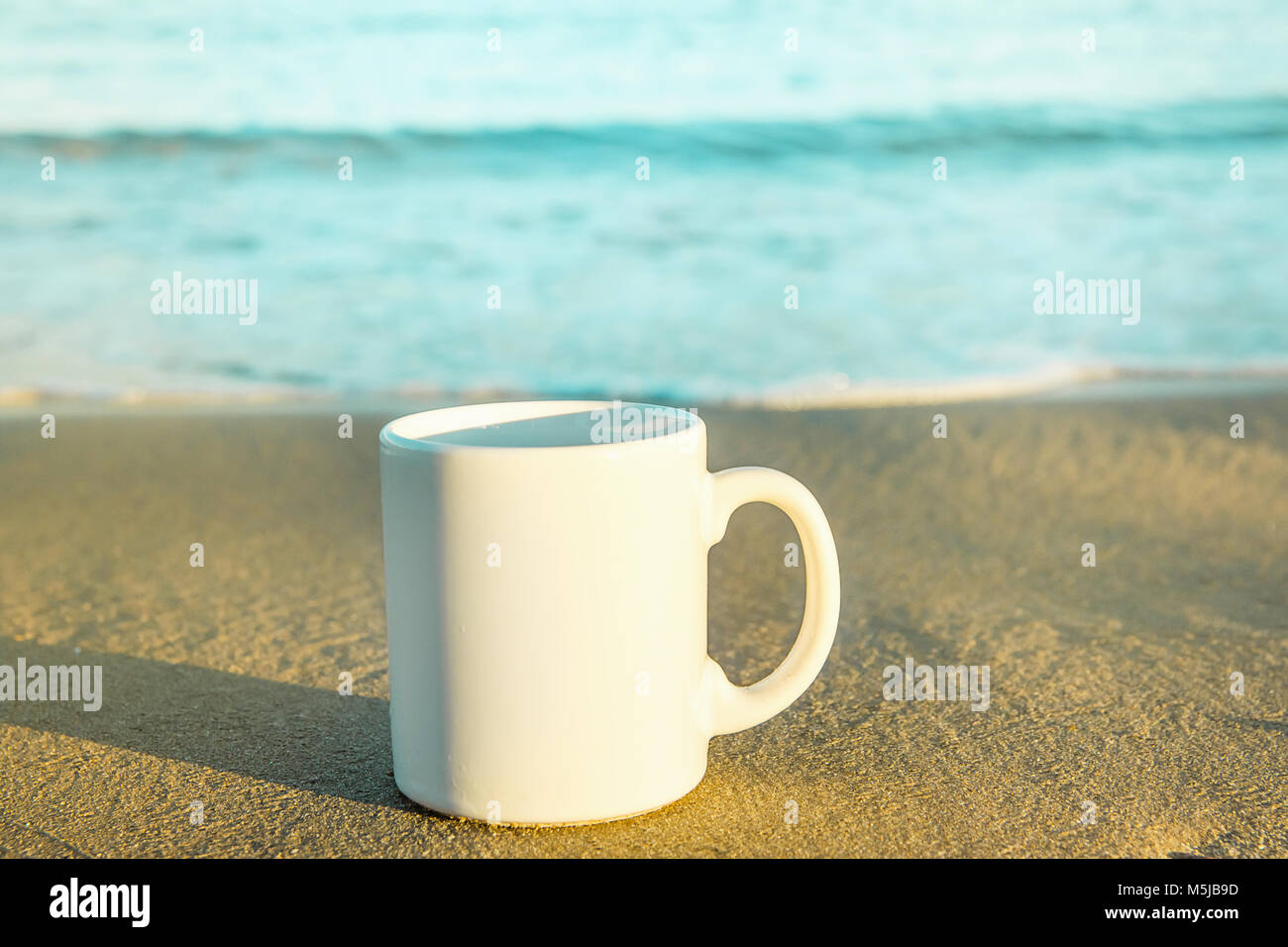 Maqueta blanca taza con un espacio vacío para ilustraciones Texto de pie  sobre la arena de la playa. Mar azul turquesa de fondo. Luz dorada del Sol  Fotografía de stock - Alamy